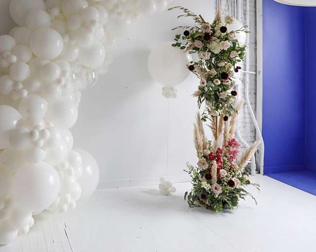 A decorated room featuring a large arrangement of white balloons on one side and a floral display with various colors on the other side.