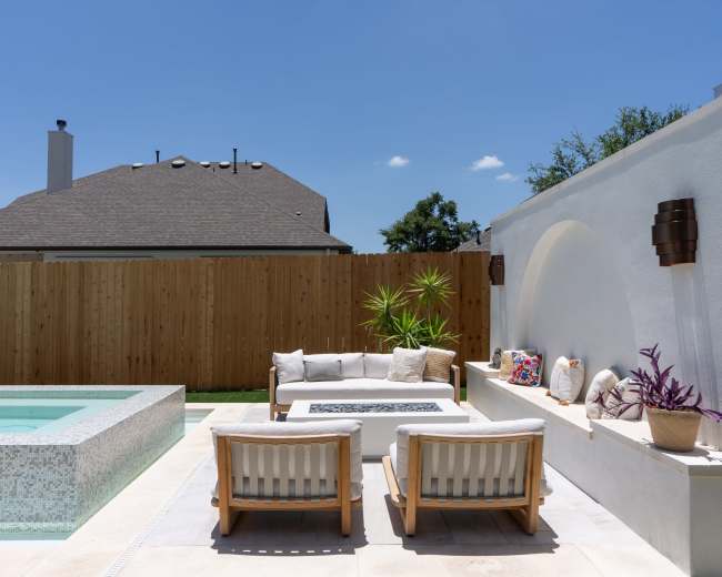 The image shows a backyard patio with a small pool, a seating area with a coffee table, and a wooden privacy fence in the background.
