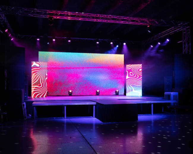 A stage is set up with colorful lighting and a large screen displaying vibrant patterns.