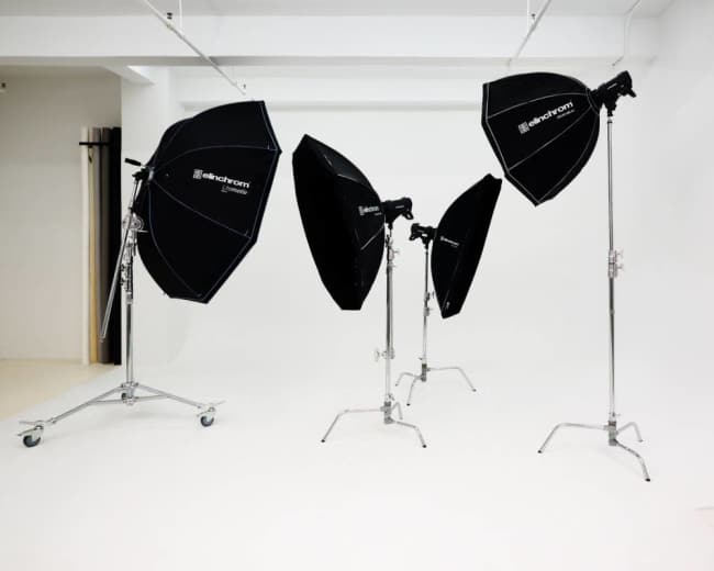 The image shows a photography studio featuring four black softbox lights on metal stands placed on a white background.