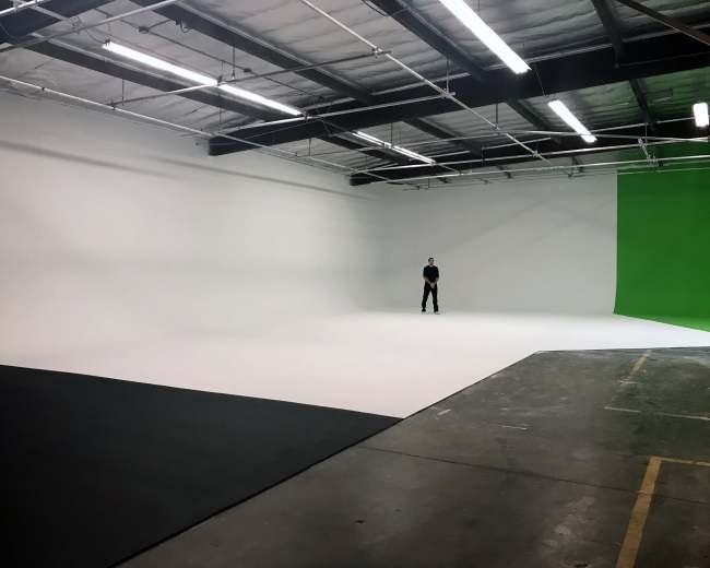 A large photography studio with a person standing in the center, surrounded by a white backdrop and a green screen.