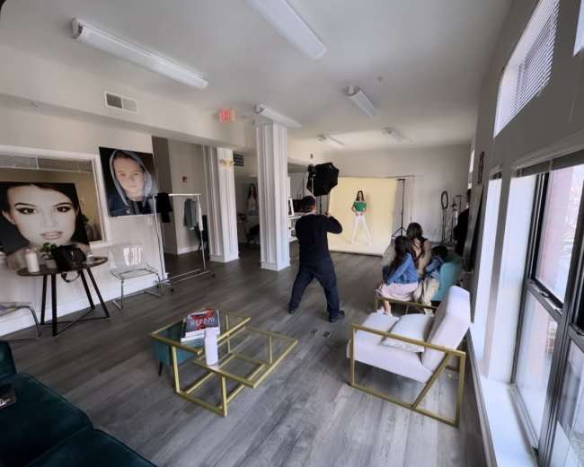 A photographer is capturing images of a model in a studio featuring large photographs on the walls and modern furnishings.
