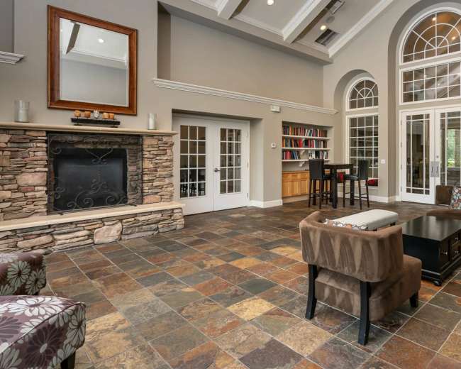 The image shows a spacious living area with a stone fireplace, large arched windows, and a mixture of seating arrangements, including a sofa and armchairs, on a tiled floor.