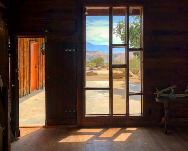 The interior of a rustic wooden cabin features large windows that provide a view of the landscape outside.
