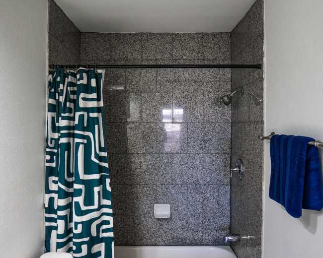 The image shows a modern bathroom with a bathtub, a patterned shower curtain, and a blue towel hanging on a rack.