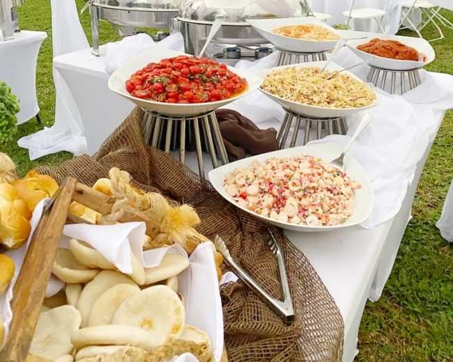 A buffet table displays various dishes, including salads and pastries, set in a garden during an outdoor event.