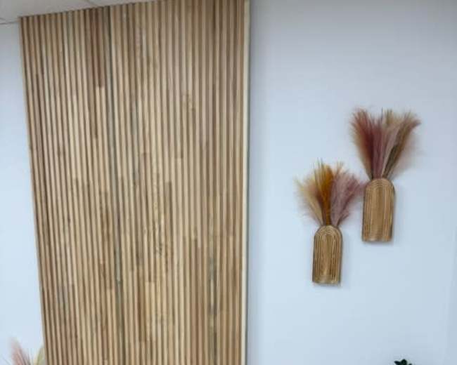 The image shows a wall covered with wooden slats, adorned with two decorative arrangements and a row of candles along the floor.