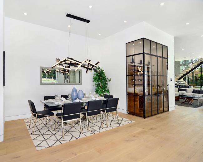 A modern dining area features a rectangular table with black chairs, a stylish light fixture above, and a glass cabinet in the background.