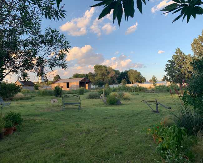 A peaceful outdoor area with grass, a few benches, and several trees under a partly cloudy sky.