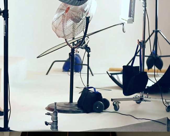 A photography studio setup featuring a fan, various lighting equipment, and backdrops on a white floor.
