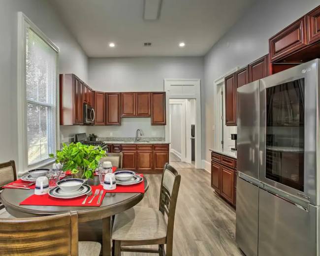 A modern kitchen features dark wooden cabinets, a dining table set for four, and stainless steel appliances.
