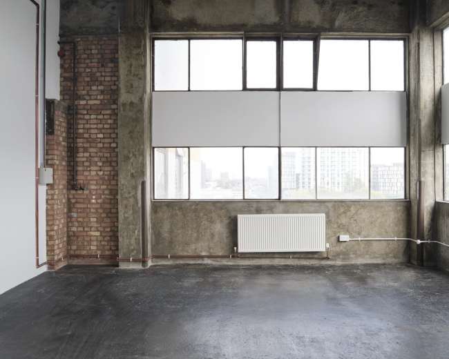 The image shows a spacious industrial-style room with large windows, exposed brick walls, and a polished concrete floor.