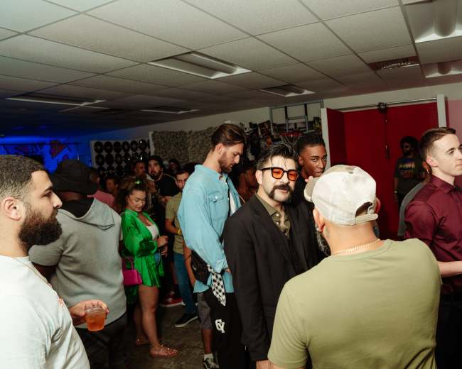 A crowd of people mingle in a brightly lit room filled with music equipment and colorful decorations.