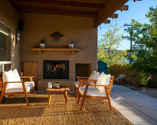 A cozy outdoor seating area features two chairs, a small round table, and a fireplace surrounded by natural light.