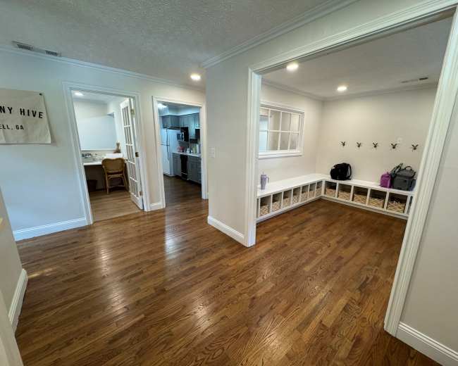 The image shows a wide hallway with a view of a kitchen and a small room featuring a bench with cubbies.