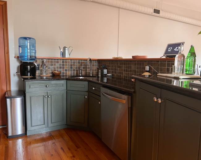 A kitchen with green cabinets, a stainless steel dishwasher, and a water dispenser next to a sink, all arranged along a tiled backsplash.