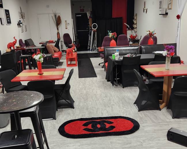 The image shows an indoor café or lounge area with red and black décor, featuring tables, chairs, and a lengthy black carpet running down the center.