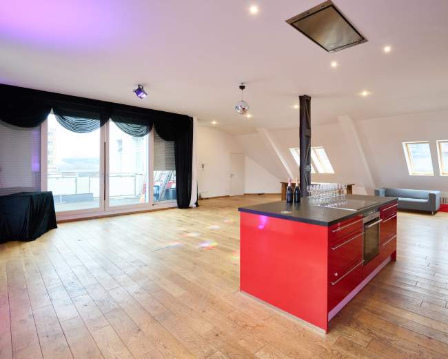 The image shows a spacious, modern apartment interior with a kitchen island, large windows, and minimal furnishings.