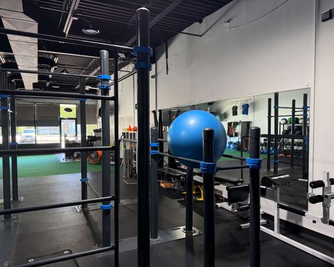 The image shows an indoor gym with exercise equipment, including a blue stability ball and a mirror reflecting various fitness apparatus.