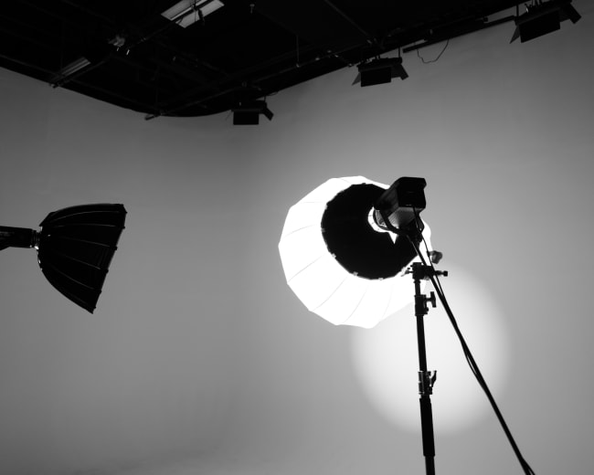 A photography studio features two light sources, including a softbox and a spotlight, against a blank backdrop.