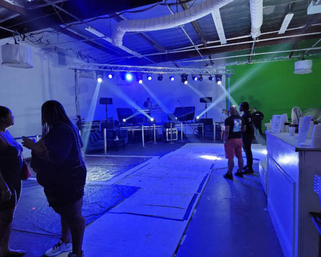 An indoor event space with a DJ setup featuring lights, a dance floor area, and people socializing.