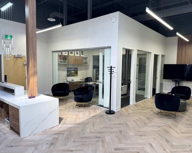 The image shows a modern office space with glass-walled meeting rooms, black chairs, and a wooden accent wall.