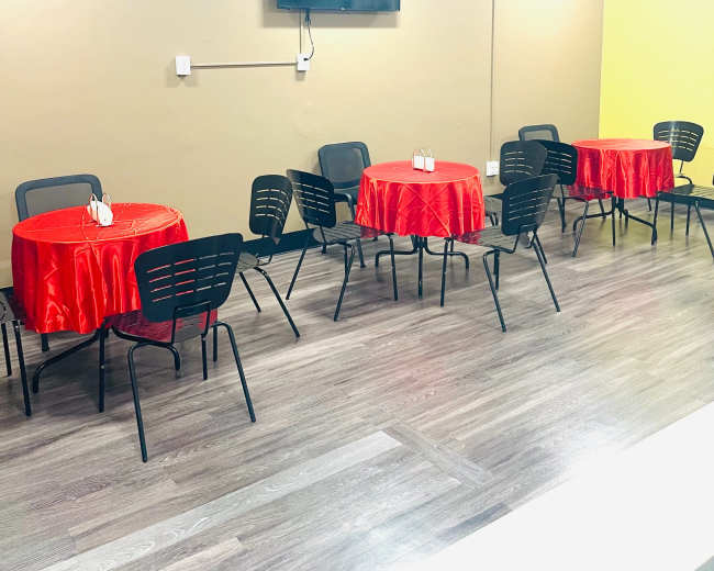 The image shows a room with several tables covered in red tablecloths and black chairs, along with a wall-mounted television.