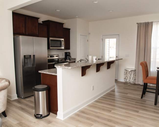 A modern open-concept kitchen features dark cabinetry, stainless steel appliances, and a granite countertop with a small dining area nearby.