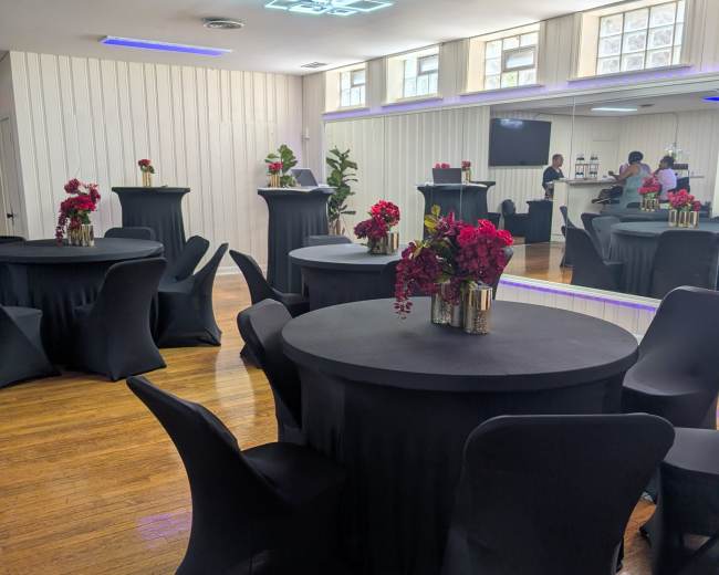 The image shows a spacious event room with black tablecloth-covered round tables adorned with floral centerpieces and sleek black chairs.