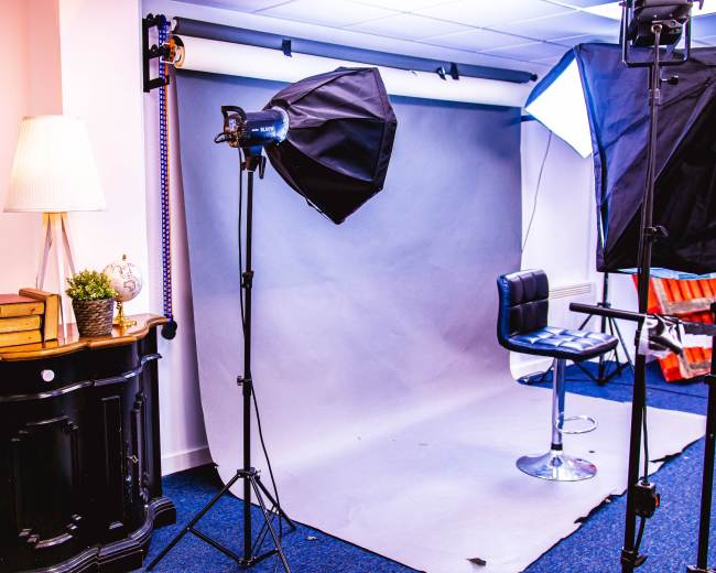 A photography studio setup with a gray backdrop, a high stool, and studio lights arranged around the space.