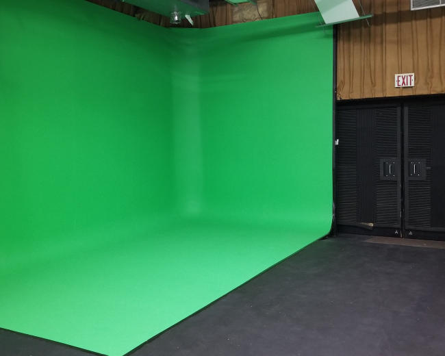 The image shows a studio space with a large green screen backdrop and dark storage doors on one side.