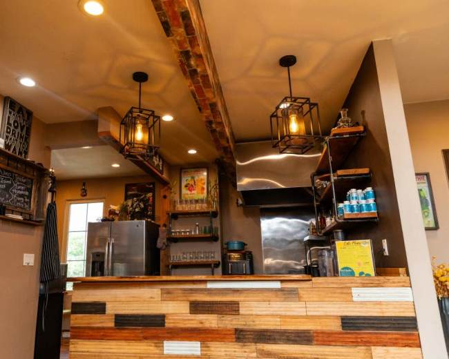The image shows a rustic café interior featuring a wooden counter, open shelving, and industrial-style light fixtures.