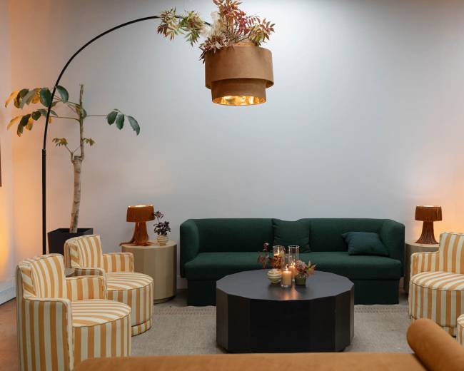 The image depicts a modern lounge area with a green sofa, striped chairs, a round black coffee table, and decorative lighting.