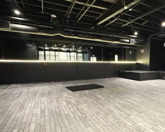 The image shows a spacious black box theater with a wooden floor and minimal lighting.