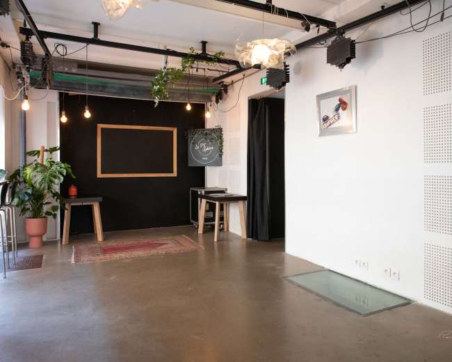 The image shows an indoor space with a black wall featuring a chalkboard, a small rug on the floor, and a potted plant beside some barstools.