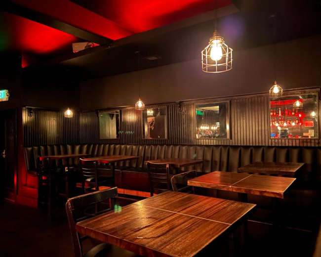 The image shows a dimly lit restaurant interior with wooden tables, black leather seating, and illuminated pendant lights hanging from the ceiling.