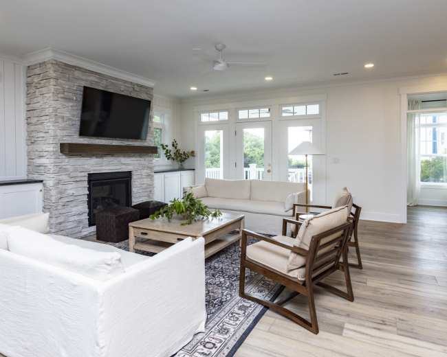 The living room features a light-colored sectional sofa, a wooden coffee table, and a stone fireplace with a mounted television above it.