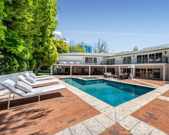 The image features a modern two-story house with a swimming pool and lounge chairs set in a landscaped outdoor area.