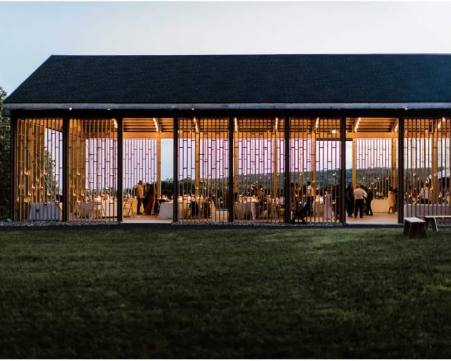 A modern building with large windows is illuminated at dusk, revealing a gathering of people dining inside.