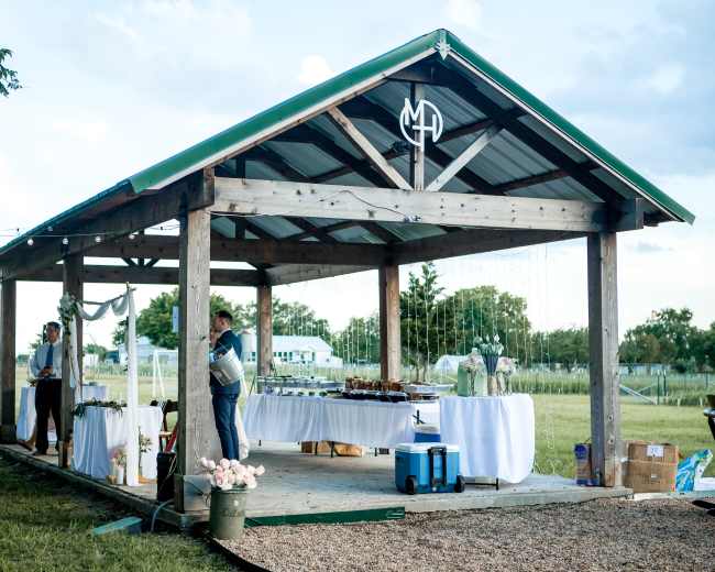 A covered outdoor pavilion with tables set for a gathering and two people preparing food.