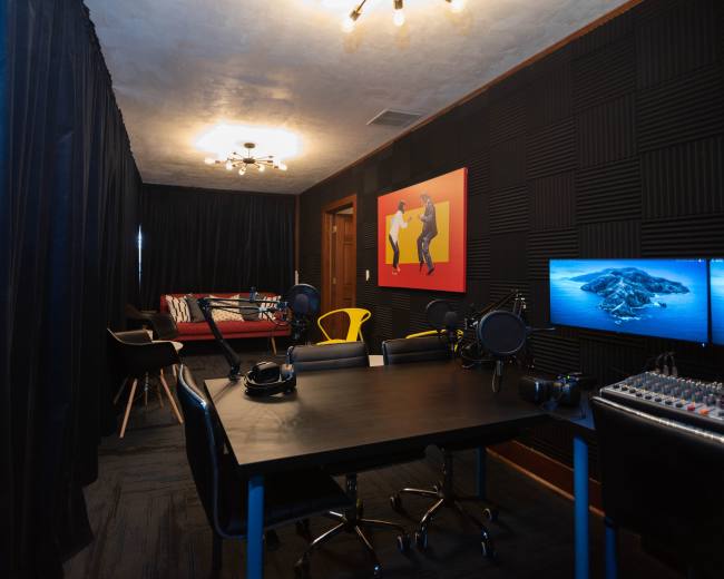 The image shows a soundproof recording studio featuring a desk with microphones, headphones, and a sound mixer, alongside seating and vibrant wall art.