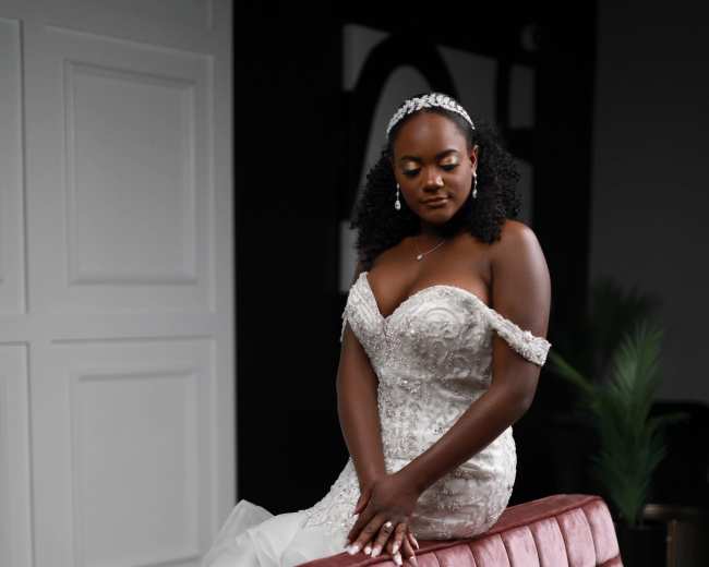 A woman in a strapless wedding gown poses gracefully on a pink velvet sofa in an indoor setting.