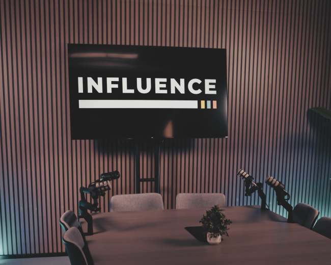 A modern conference room features a large table surrounded by chairs, with a screen displaying the word "INFLUENCE" on the wall.