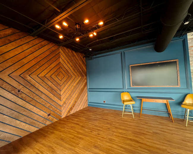 The image shows a modern interior space featuring a patterned wooden wall, a blue accent wall, a wooden table, and two yellow chairs.