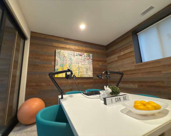 The image shows a modern workspace featuring a white table, turquoise chairs, a large piece of abstract art on the wall, and a decorative bowl of oranges.