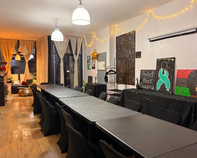 The image shows a brightly lit room with several long tables, black chairs, and decorations that include banners and artwork on the walls.