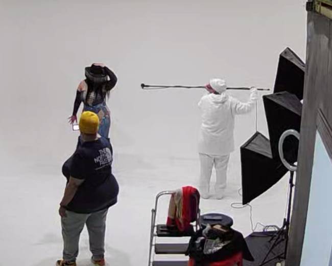 A model poses in a studio while a photographer adjusts equipment in the background.
