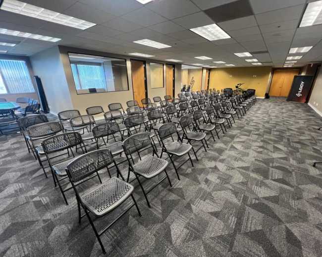 The image shows a room arranged with rows of black folding chairs, set up for an event or meeting.