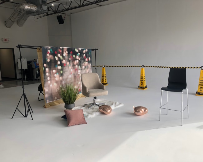 A photography setup with a backdrop of blurred lights, two chairs, a small plant, decorative pillows, and caution cones marking off the area.