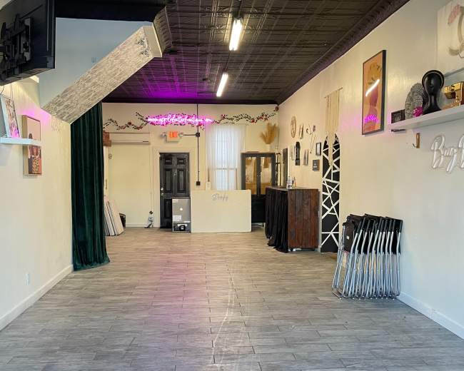 The image shows an empty, well-lit indoor space with a tiled floor, green curtains on one side, and various decor items on the walls.